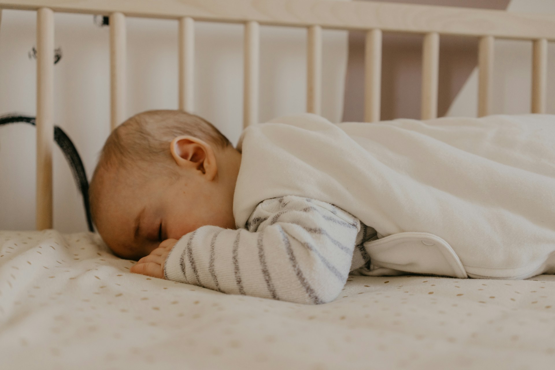 Baby sleeping peacefully on its side in a wooden crib, wrapped in a soft white blanket